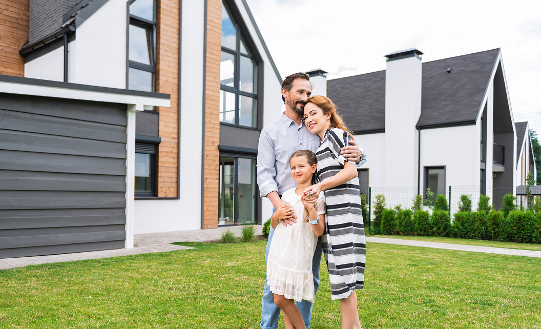 Famille heureuse devant une maison neuve moderne avec jardin, symbole de réussite et de construction immobilière en Île-de-France
